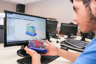 Jeune homme avec un prototype 3D dans les mains devant un ordinateur